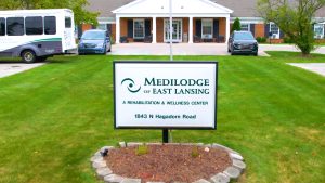 Sign board of Medilodge of East Lansing. Two car in the background.